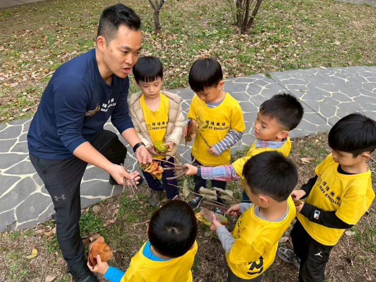 Kindergarten children collecting fall leaves outdoors, naming colors and shapes in English